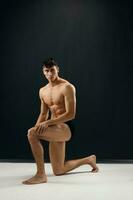 athletic man with muscular naked body in dark panties is kneeling photo