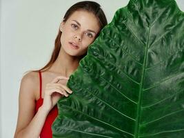 woman in a red t-shirt stands behind a green leaf of a palm tree on a light background photo