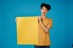 guy with curly hair yellow posters in hands Copy Space blue background studio photo