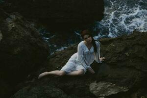 Barefoot woman in a wedding dress lying on a stone in a white dress lying on her back on a rocky seashore photo