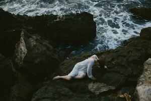 Barefoot woman in a white dress lying on a stone in a white dress landscape photo