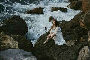 barefoot woman in white dress sits on a stone with wet hair photo