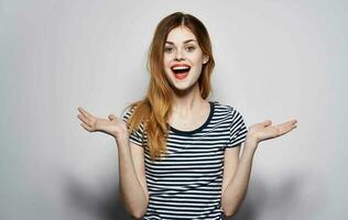 pretty woman in striped t-shirt throws up her hands emotions red lips studio photo