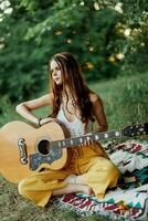 A girl in eco-clothing hippie sitting with a guitar and looking at a sunset in the summer photo