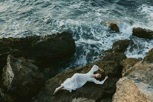 beautiful young woman in a white dress lying on a stone in a white dress view from above photo