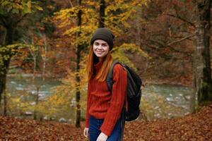 woman tourist in a sweater hat with a backpack near tall trees in autumn in the forest photo