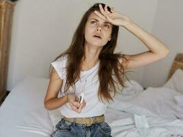 woman holds her hand on her forehead thermometer high temperature in the bedroom photo