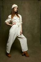 a beautiful woman in a jumpsuit and a boot holds her hand on a belt on a brown background in full growth photo