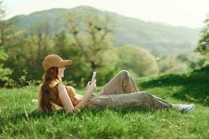 Top view A young female freelance student in a yellow cap, top, and green pants is working on her cell phone sitting on the green grass in the park. Lifestyle and concept of a young healthy society photo