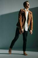 A man in jeans and a brown jacket looking to the side on a gray background bottom view photo