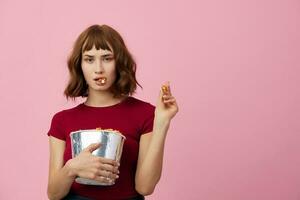 Excited confused cute redhead lady in red t-shirt with popcorn ready for movie evening posing isolated on over pink studio background. Copy space Banner. Fashion Cinema concept. Entertainment offer photo