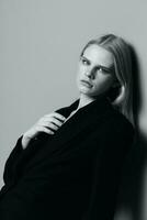 Portrait of a beautiful blonde in a classic jacket leaning against the wall in the studio. Black and white style. Concept for clothing brands photo