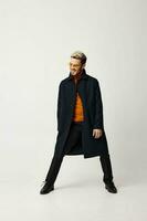 blond man in fashionable clothes spread his legs and light background orange sweater pants photo