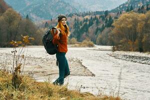 mujer en pantalones y un chaqueta con un mochila cerca el río en el montañas paisaje naturaleza foto