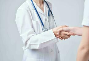 Doctor and patient shake hands with each other on a light background cropped view photo