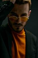 a brutal guy with glasses and a black jacket orange sweater dark background photo