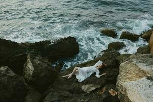 woman in a secluded spot on a wild rocky coast in a white dress view from above photo