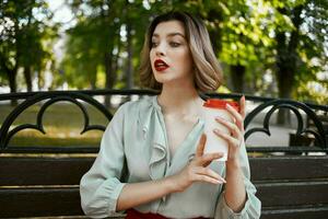 rubia sentado en un parque banco un taza de café calle descanso foto