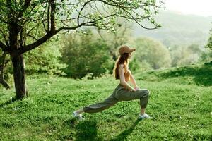 un joven atlético mujer lo hace Deportes extensión en naturaleza en el parque. verde verano paisaje en el luz de sol en naturaleza foto