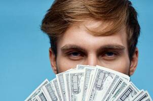 a man with a wad of money covers his face close-up blue background photo