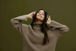 mujer en un suéter escuchando a música con auriculares divertido aislado antecedentes foto