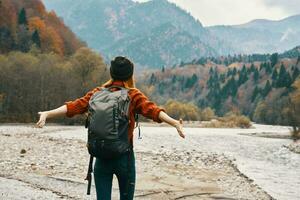 a traveler with a backpack in a sweater and jeans are resting in the mountains in nature near the river in autumn photo