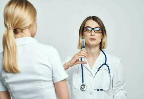 A nurse doctor in a medical gown explains something to a patient in a white T-shirt photo