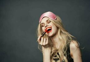 Drunk blonde with bright makeup on her face red lips and a pink sleep mask photo