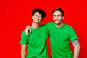 two friends in green t-shirts hugs fun red background photo