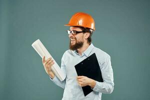 un masculino ingeniero en un naranja difícil sombrero con documentos en el manos de construcción dibujos foto