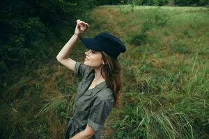 Woman in the forest Green jumpsuit black cap hand over head fresh air photo