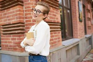 bonito mujer con lentes caminando alrededor el ciudad con un libro estilo de vida foto