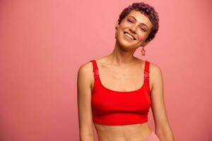 Fashion portrait of a woman with a short haircut of purple color and a smile with teeth in a red top on a pink background dancing happily photo