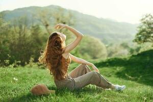 joven mujer con largo rojo pelo relajante en ropa de deporte en el césped en un naturaleza parque, volador cabello, el concepto de un sano estilo de vida y preocupación para el ambiente y ecología foto