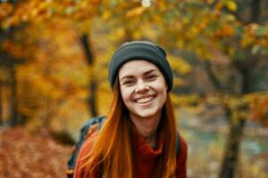 portrait of a beautiful woman in a hat sweater with a backpack on her back in the autumn forest in nature photo
