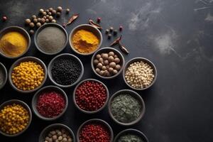 View from above of numerous spices in small bowls on a dark slate plate with copy space created with technology. photo