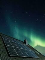 Solar panels producing clean energy on a roof of a residential house with aurora borealis in the background. photo