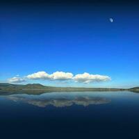 Reflection of clouds on the lake with half moon in the blu sky photo