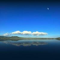 Reflection of clouds on the lake with half moon in the blu sky photo