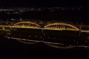 brillante luces, puentes con arcos, noche ciudad. un la carretera puente a través de el río, tomado desde un zumbido. foto