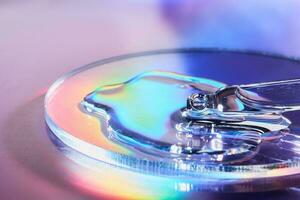 Pipette with sample of cosmetic product in petri dish on holographic background, iridescent highlights, selective focus photo