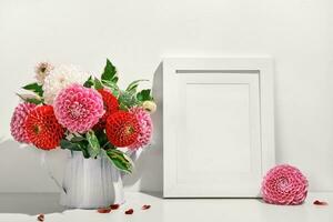 Mockup with photo frame and Autumn dahlias flowers bouquet on white table. Wall table background, trendy shadows