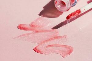 Smears of shining lip gloss and lip gloss brush on pink background, hard shadows photo