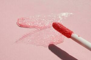 Smears of shining lip gloss and lip gloss brush on pink background, hard shadows photo