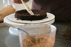 Woman pastry chef impregnates chocolate sponge cake on stand, close-up. Cake making process, Selective focus photo