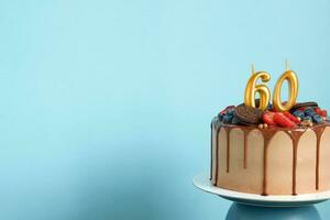 Chocolate birthday cake with berries, cookies and number sixty golden candles on blue wall background, copy space photo