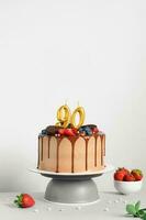 Chocolate birthday cake with berries, cookies and number ninety golden candles on White background, copy space photo