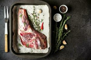 Raw fresh Lamb Meat in baking tray, herbs and fork on black stone background photo