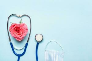 Pink rose heart, stethoscope and protective mask on blue background. Thank you doctor and nurse day concept photo
