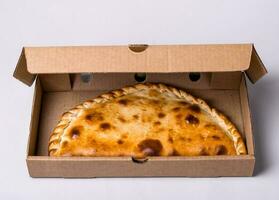 Closed pizza calzone in packing box on gray background photo